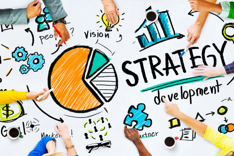 Image of a group of people collaborating on a whiteboard with various diagrams and illustrations related to strategy development.